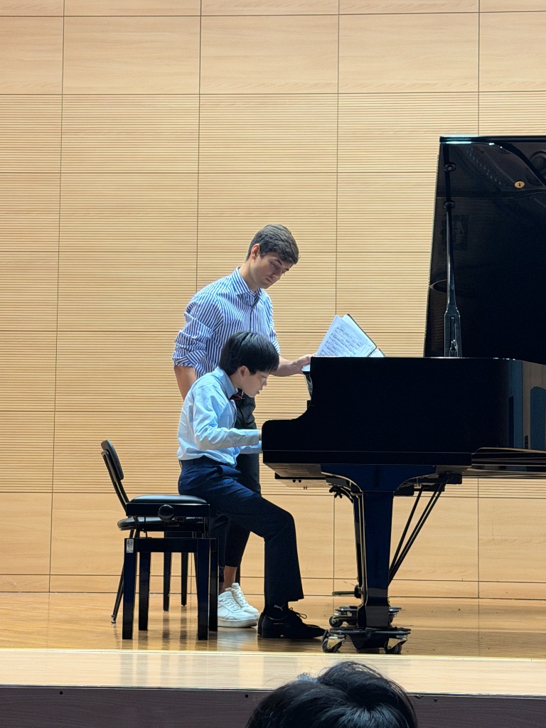 Artem Alexanian helping a student with sheet music at the piano