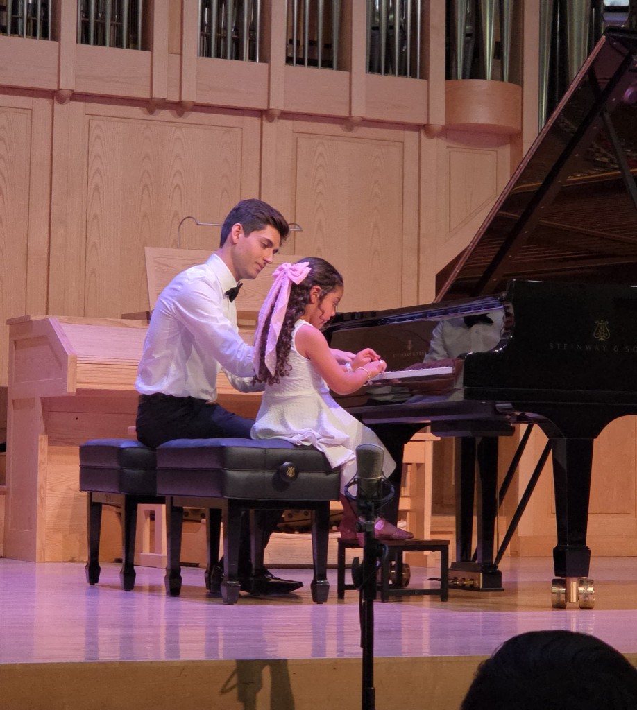 Young student and performer playing a piano duet at a recital on a Steinway grand piano