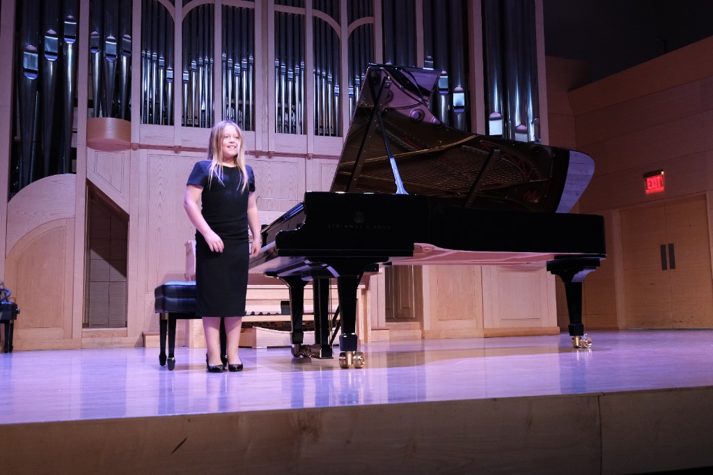 Young student smiling beside a Steinway grand piano after recital